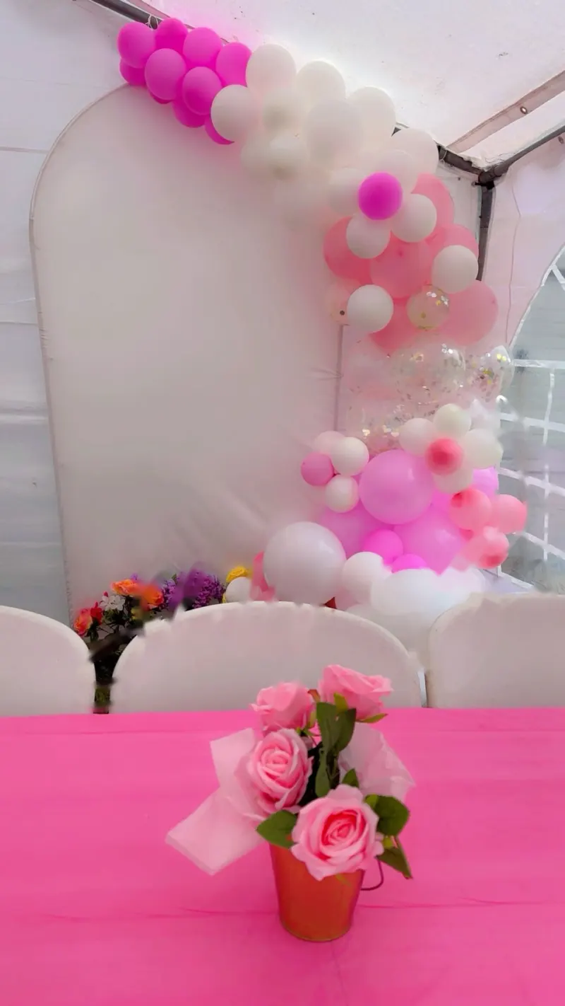 Arco de globos rosas y blancos junto a un panel en arco y un centro de mesa de rosas