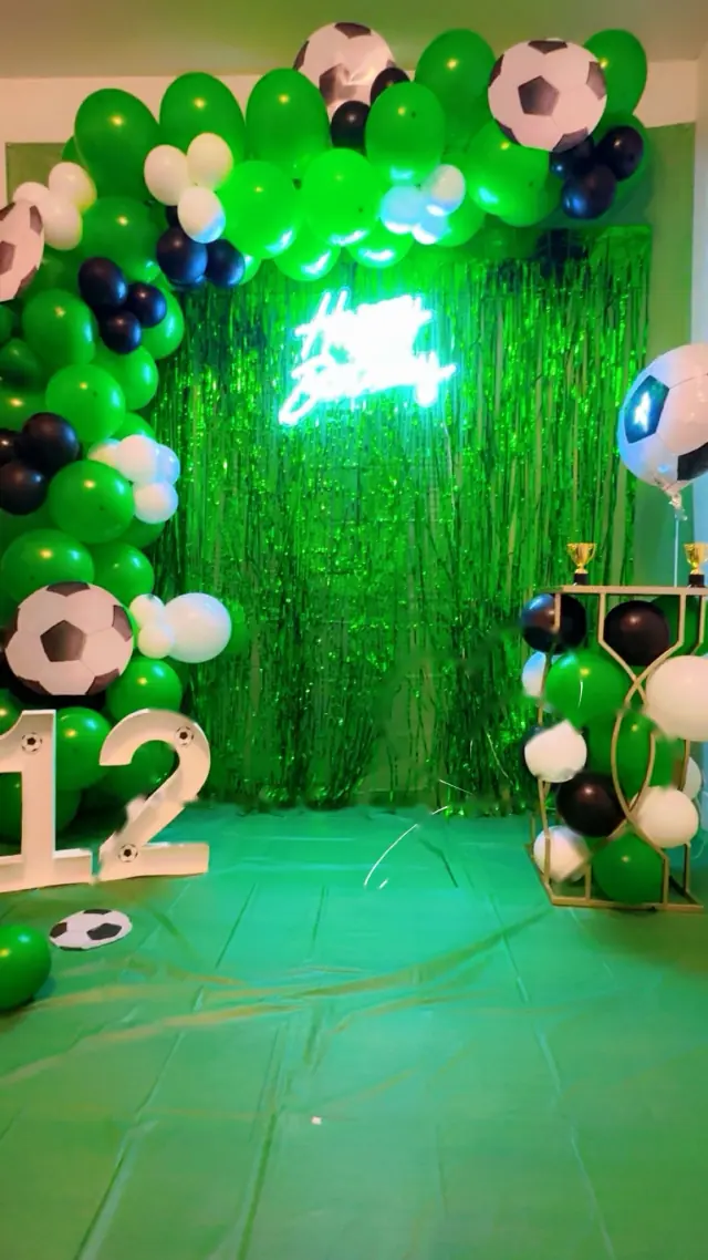 Arco de globos verdes con letrero de neón y balones de fútbol