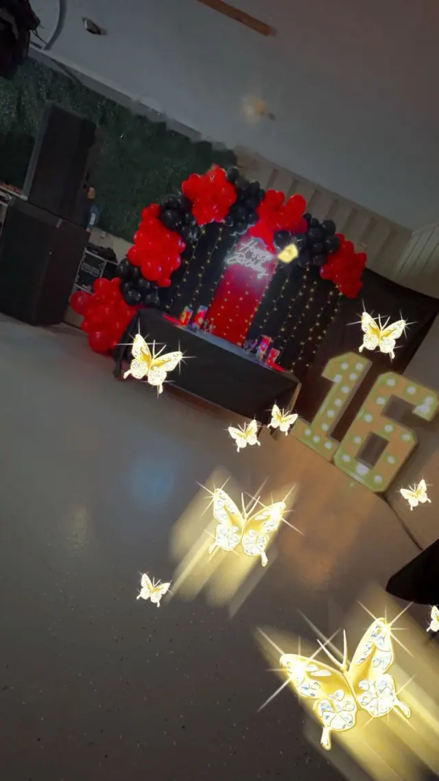 Mesa de XV años con globos rojos y negros, número 16 y mariposas de luz
